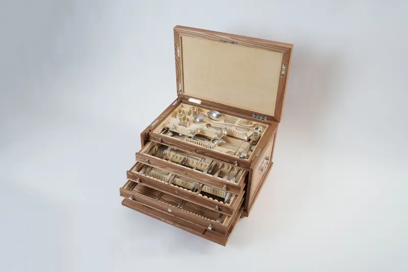 An open elm and oak cutlery canteen with pulled‑out drawers and silver cutlery
